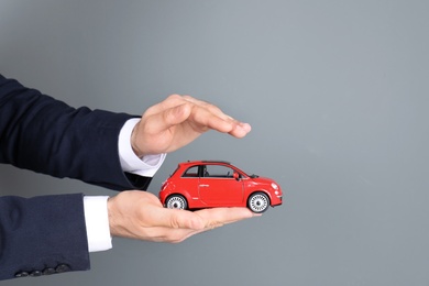 Male insurance agent holding toy car on grey background, closeup. Space for text