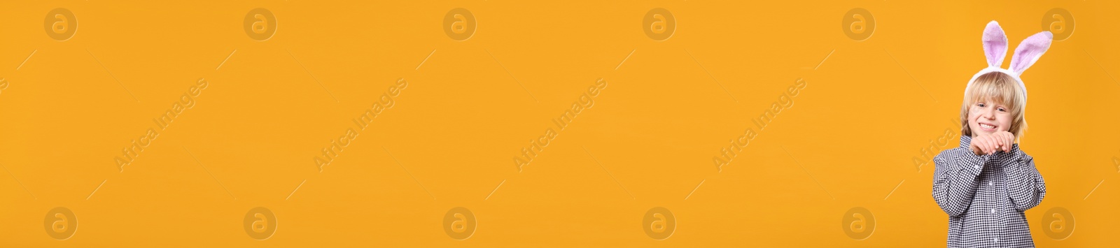 Image of Happy little boy with bunny ears headband on orange background, space for text. Easter celebration. Banner design