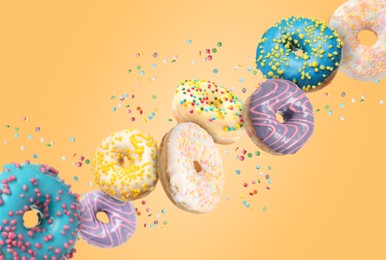 Many sweet tasty donuts with sprinkles falling on pale orange background