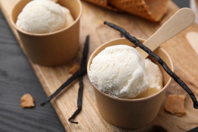 Photo of Paper cups with delicious ice cream and vanilla pods on grey wooden table, closeup