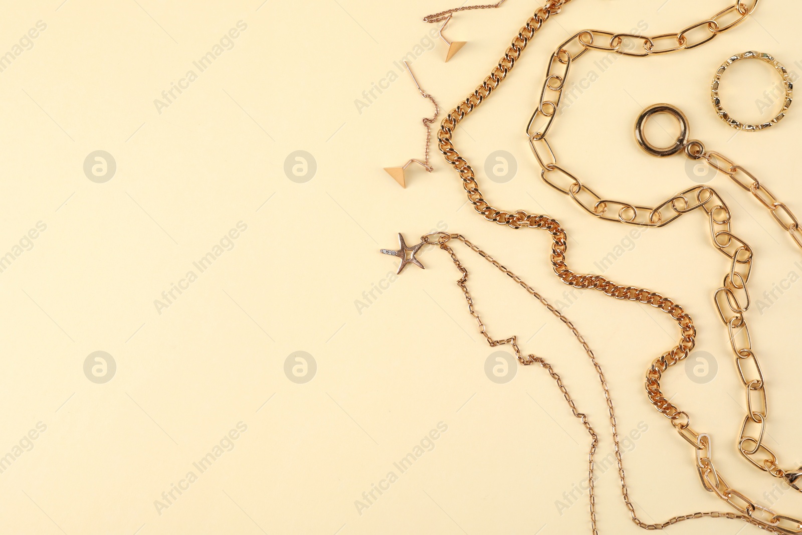 Photo of Metal chains and other different accessories on beige background, flat lay with space for text. Luxury jewelry