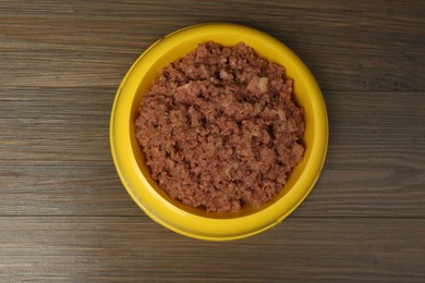 Wet pet food in feeding bowl on wooden background, top view