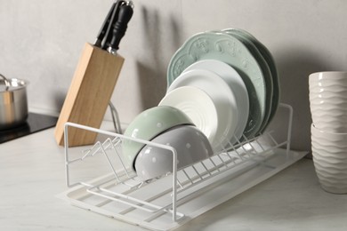 Photo of Drainer with different clean dishware on white table indoors