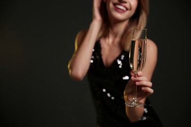 Photo of Beautiful woman with glass of champagne on dark background, closeup. Space for text