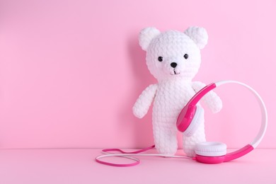 Photo of Baby songs. Toy bear and headphones on pink background, space for text