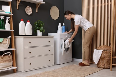 Beautiful woman putting shirt into washing machine in laundry room