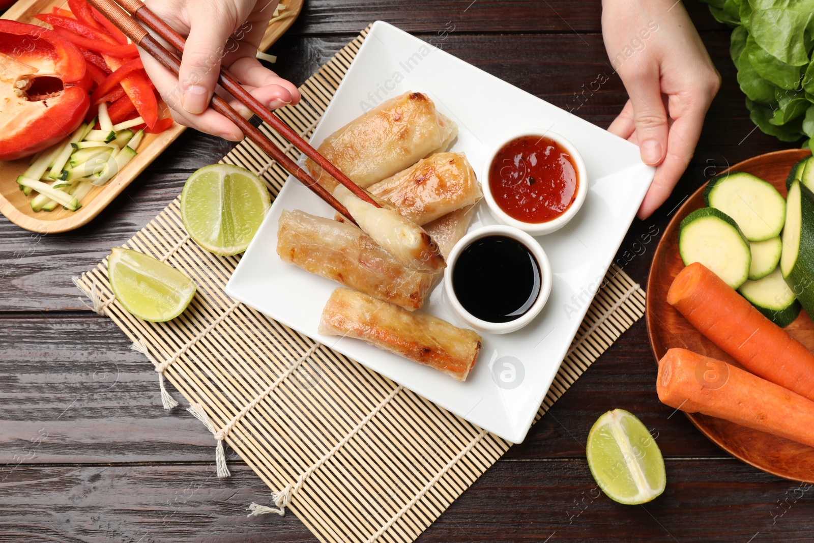 Photo of Woman eating tasty fried spring rolls at wooden table, flat lay