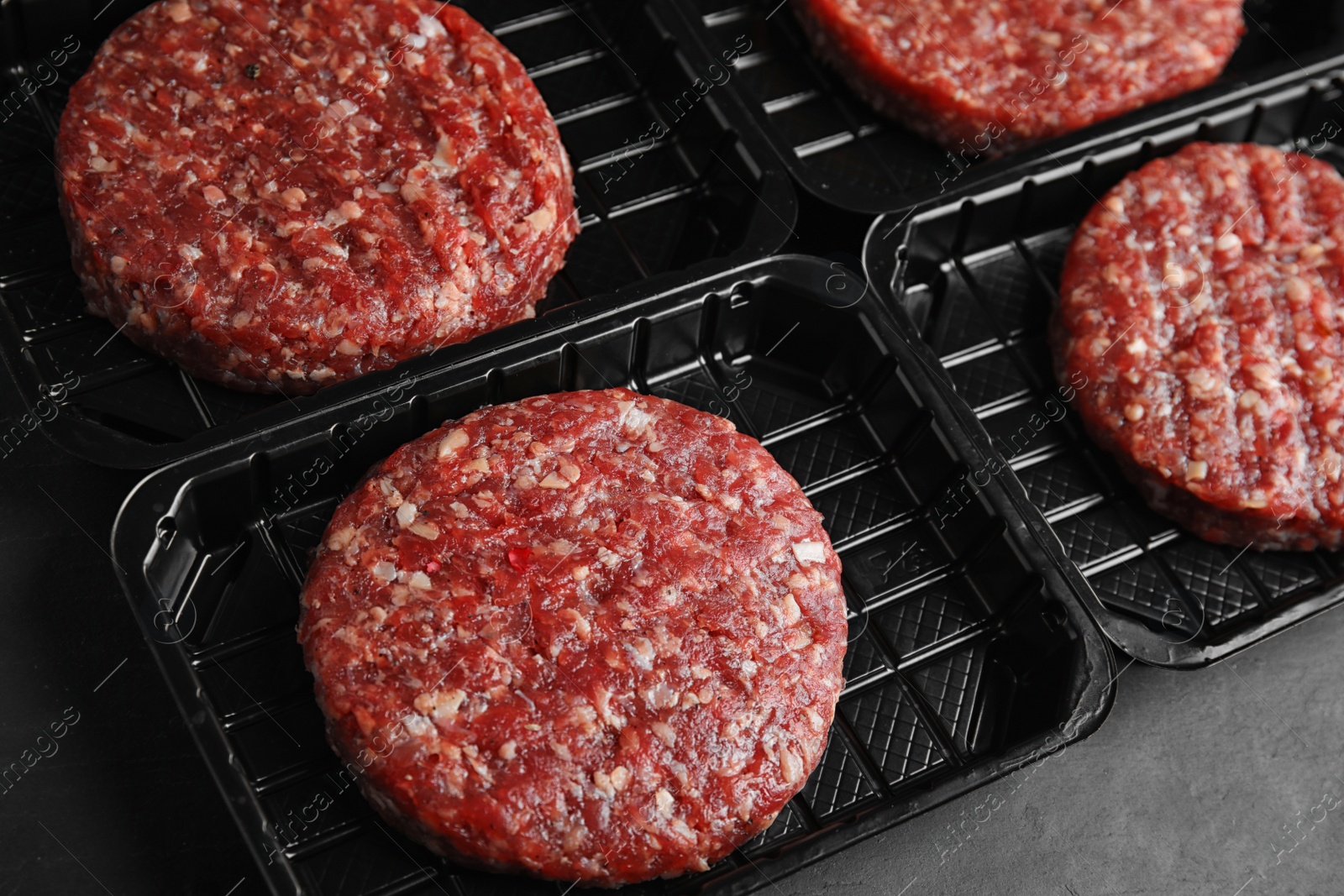 Photo of Plastic containers with raw meat cutlets for burger on grey table