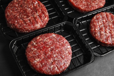 Plastic containers with raw meat cutlets for burger on grey table