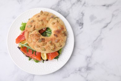 Photo of Tasty bagel with salmon and tomatoes on white marble table, top view. Space for text