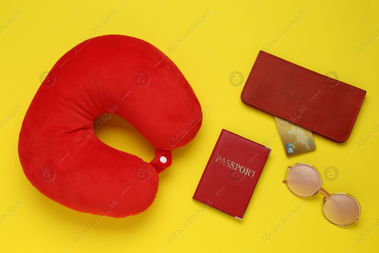 Photo of Red travel pillow, wallet with credit card, passport and sunglasses on yellow background, flat lay