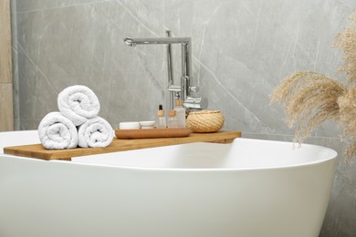 Photo of Rolled bath towels and personal care products on tub tray in bathroom