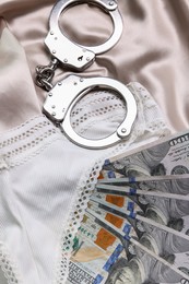 Photo of Prostitution concept. Women`s panties, dollar banknotes and handcuffs on beige silk, flat lay