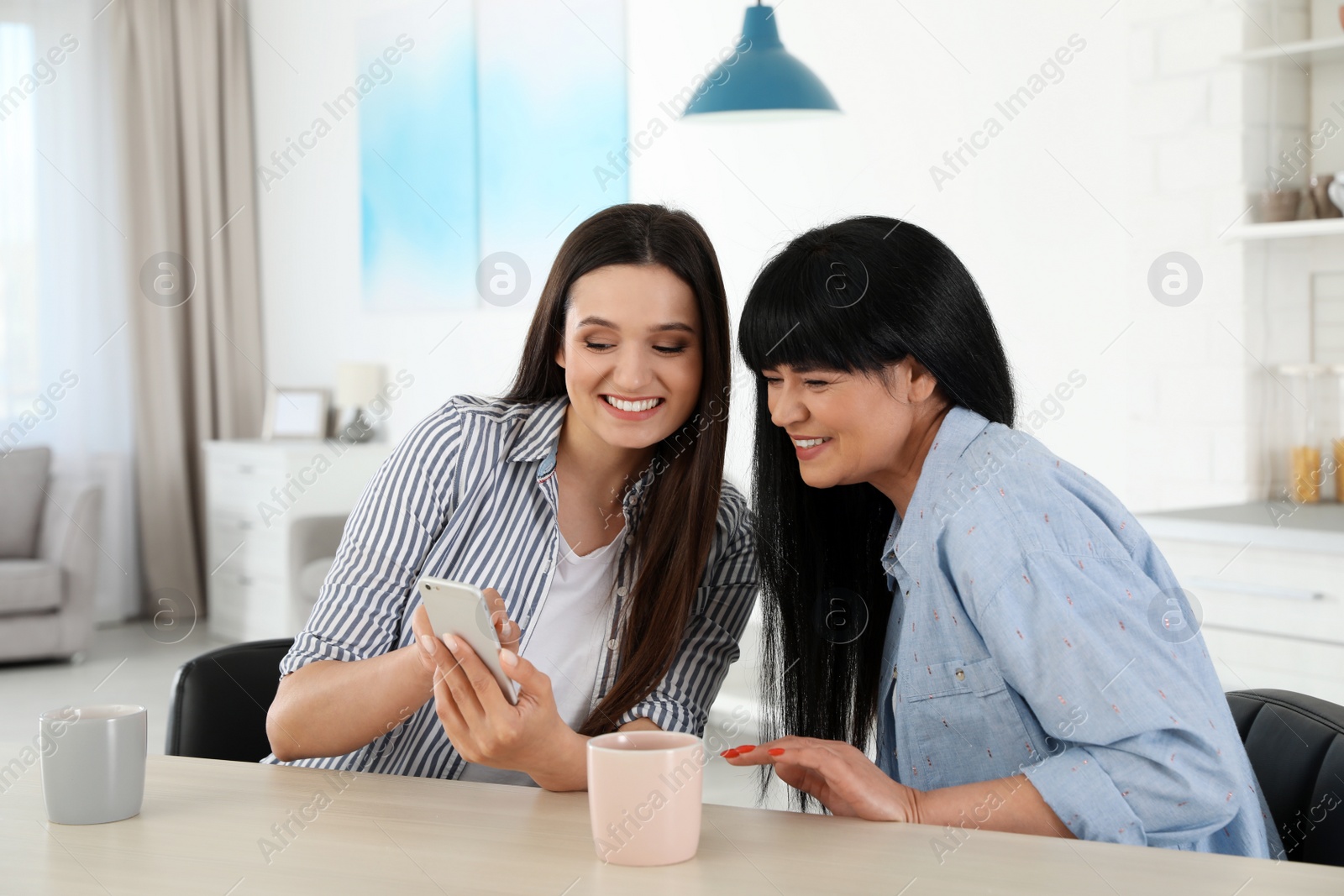 Photo of Young woman and her mature mother with smartphone at table indoors