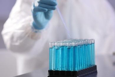 Scientist taking sample of light blue liquid in laboratory, closeup