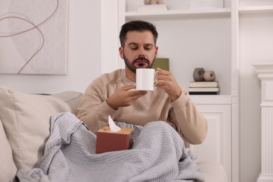 Photo of Sick man with tissues on sofa at home. Cold symptoms