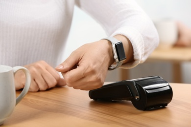 Woman using terminal for contactless payment with smart watch in cafe