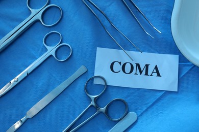 Photo of Card with word Coma and surgical instruments on table, flat lay