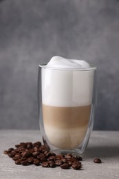 Photo of Aromatic latte macchiato in glass and coffee beans on light grey table