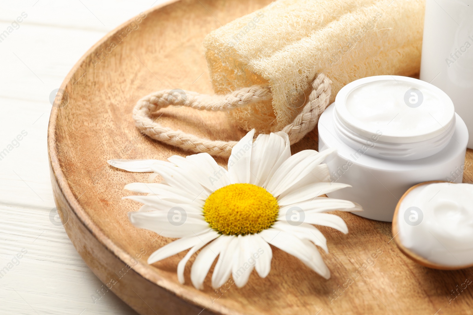 Photo of Cosmetic products, chamomile and loofah on wooden plate, closeup