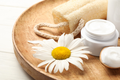 Photo of Cosmetic products, chamomile and loofah on wooden plate, closeup