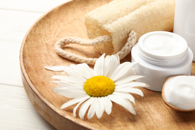 Cosmetic products, chamomile and loofah on wooden plate, closeup