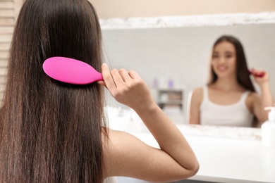 Beautiful young woman with hair brush looking into mirror in bathroom