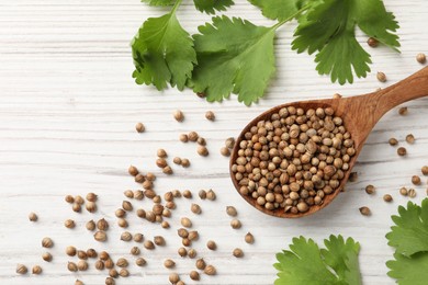 Spoon with dried coriander seeds and green leaves on wooden table, flat lay