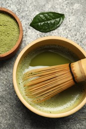 Photo of Cup of fresh matcha tea with bamboo whisk and green powder on grey table, flat lay