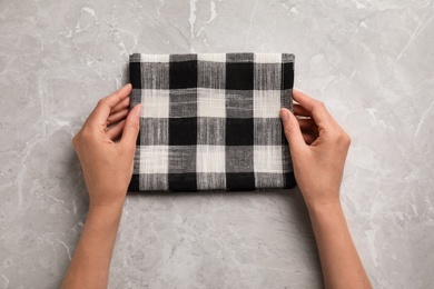 Woman with checkered kitchen towel on marble background, top view