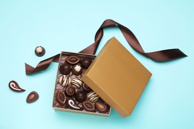 Photo of Open box of delicious chocolate candies on light blue background, flat lay