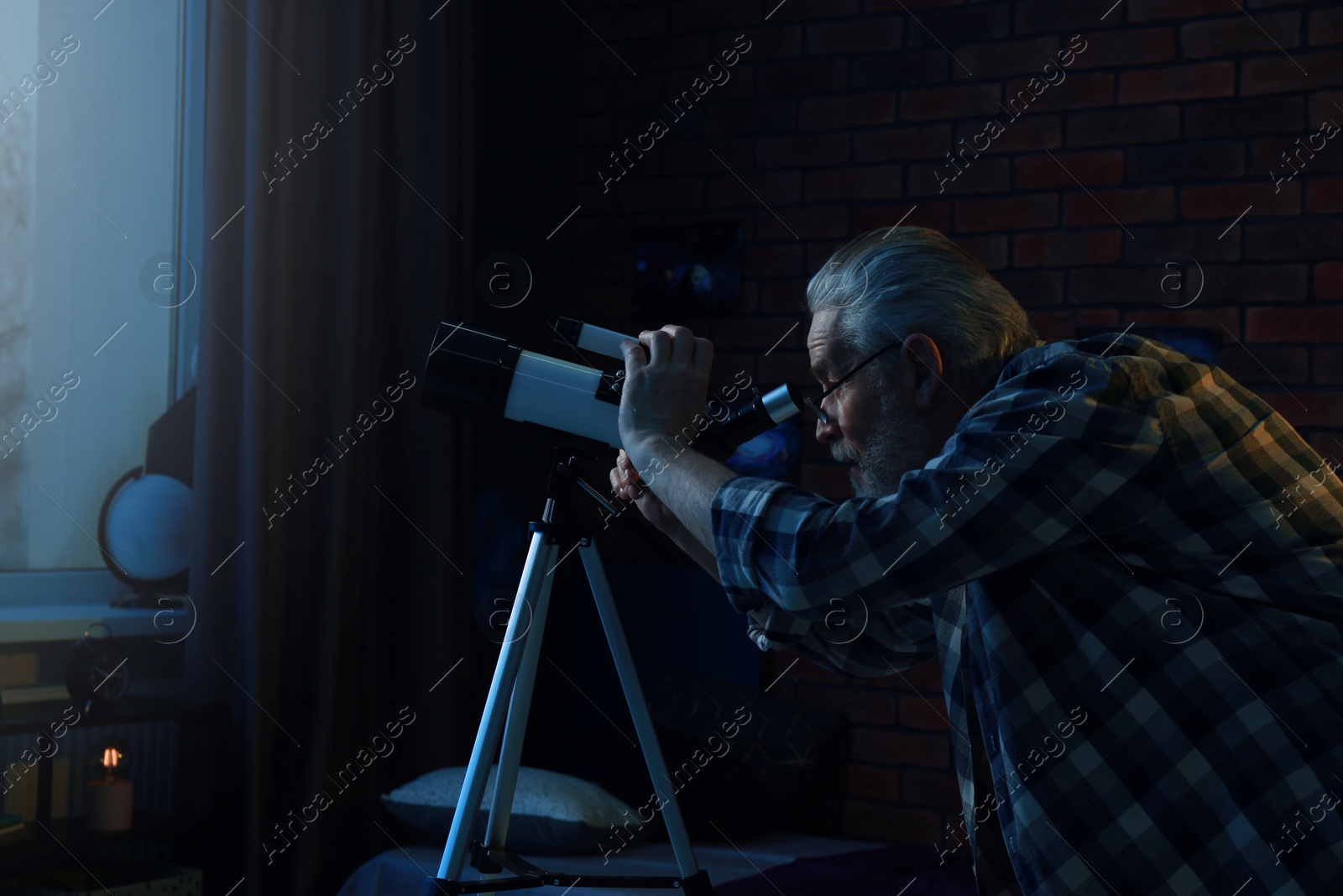 Photo of Senior man looking at stars through telescope in room