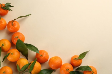 Photo of Fresh ripe tangerines with green leaves on beige background, flat lay. Space for text