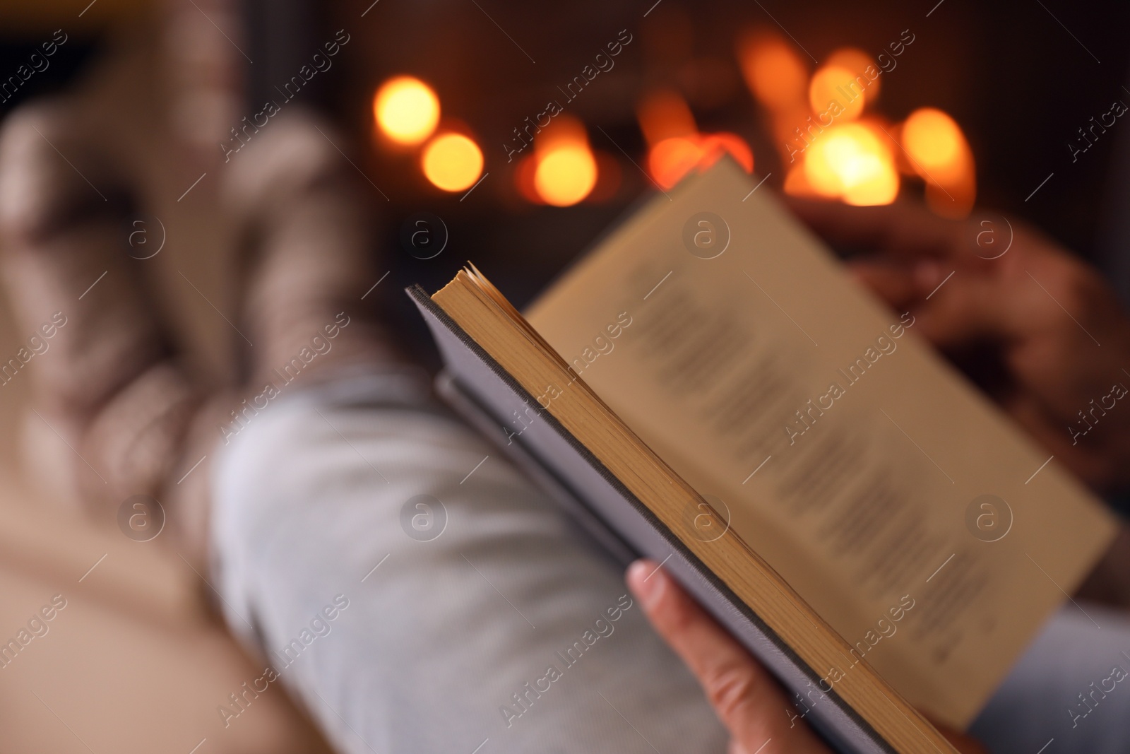 Photo of Man reading book near fireplace at home, closeup