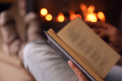 Photo of Man reading book near fireplace at home, closeup