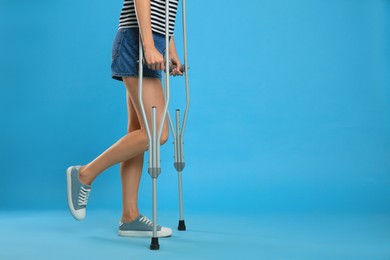 Photo of Young woman with axillary crutches on light blue background, closeup. Space for text