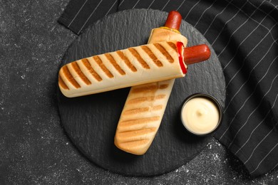 Photo of Tasty french hot dogs and dip sauce on black table, top view