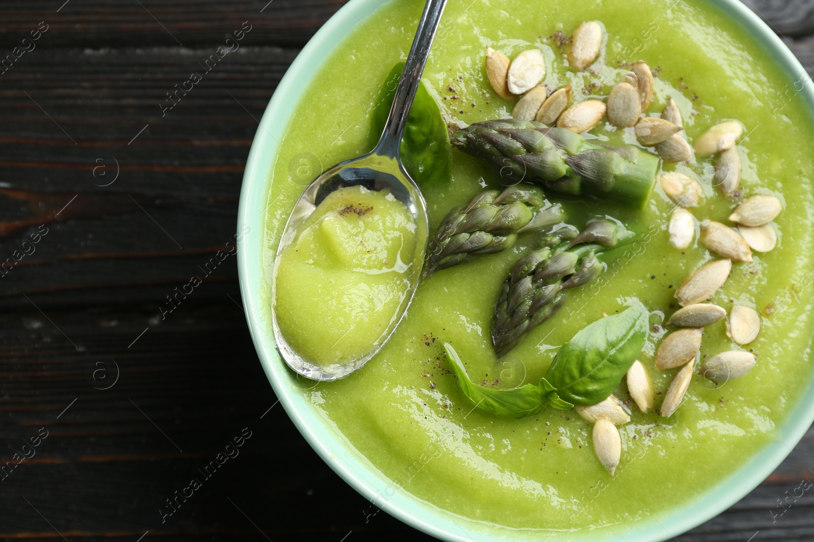 Photo of Delicious asparagus soup in bowl on black wooden table, top view