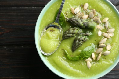 Photo of Delicious asparagus soup in bowl on black wooden table, top view