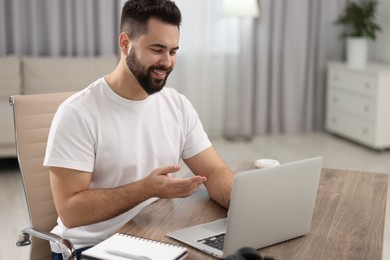 Photo of Young man using video chat during webinar at table in room