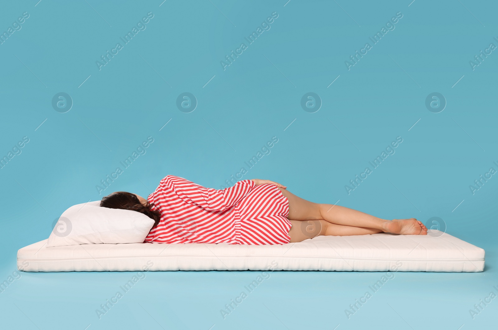 Photo of Young woman sleeping on soft mattress against light blue background, back view