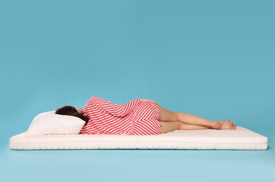 Photo of Young woman sleeping on soft mattress against light blue background, back view