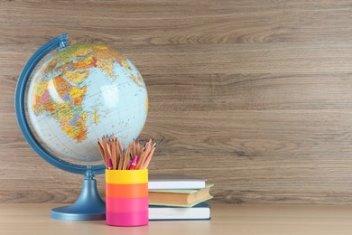 Photo of Globe, books and school supplies on wooden table, space for text. Geography lesson