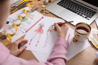 Fashion designer drawing sketch at wooden table, closeup