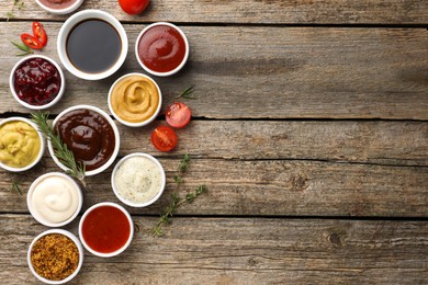 Different tasty sauces in bowls and ingredients on wooden table, flat lay. Space for text