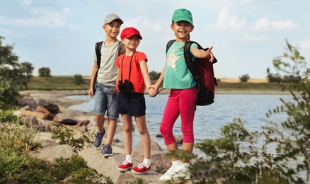Image of Cute little children with backpacks and binoculars on rock near river. Camping trip