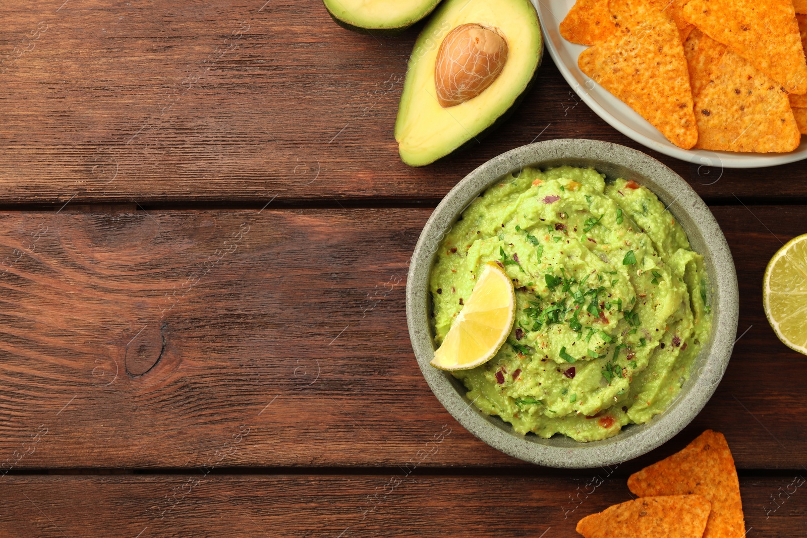 Photo of Bowl of delicious guacamole and nachos chips on wooden table, flat lay. Space for text