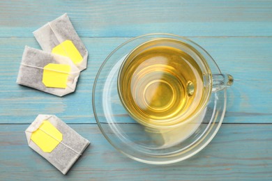 Photo of Tea bags and cup with hot drink on light blue wooden table, top view