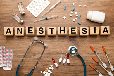 Photo of Word Anesthesia made of wooden cubes, stethoscope and drugs on table, flat lay