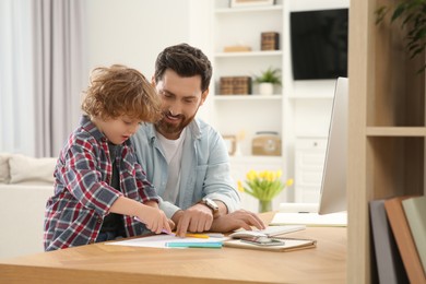 Photo of Man working remotely at home. Father looking onto his son's drawing at desk